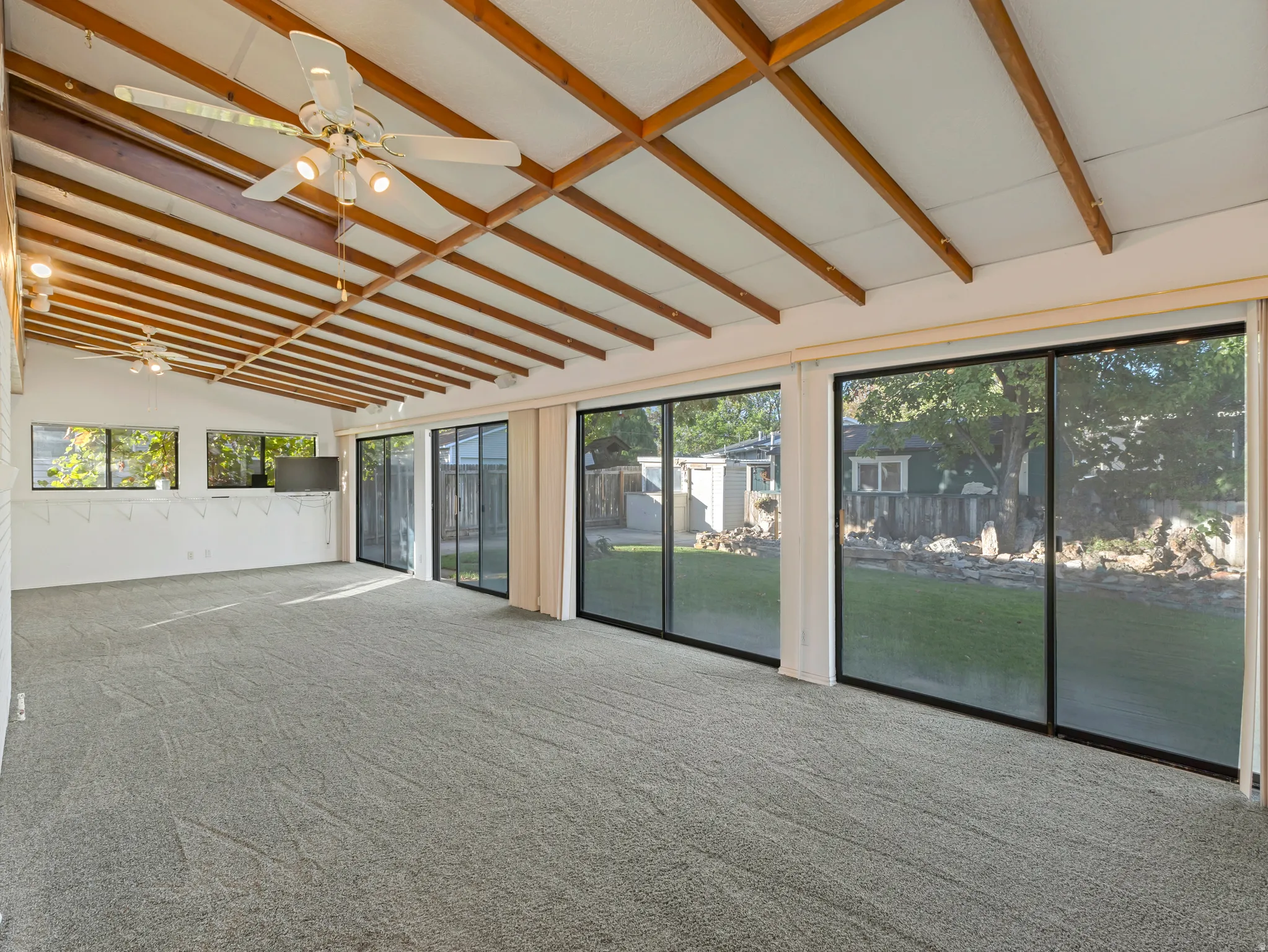 Spacious room with a vaulted ceiling featuring exposed wood beams and two ceiling fans
