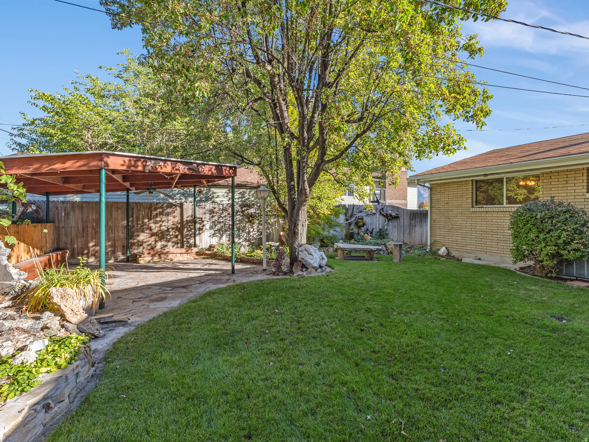 Expansive backyard featuring a covered patio, established tree, manicured lawn, and perimeter fencing