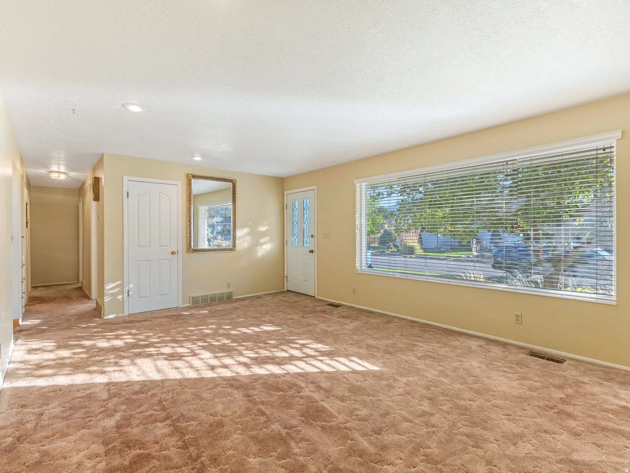 Expansive main living area featuring a large picture window with horizontal blinds, carpet flooring, recessed lighting, and a white paneled door