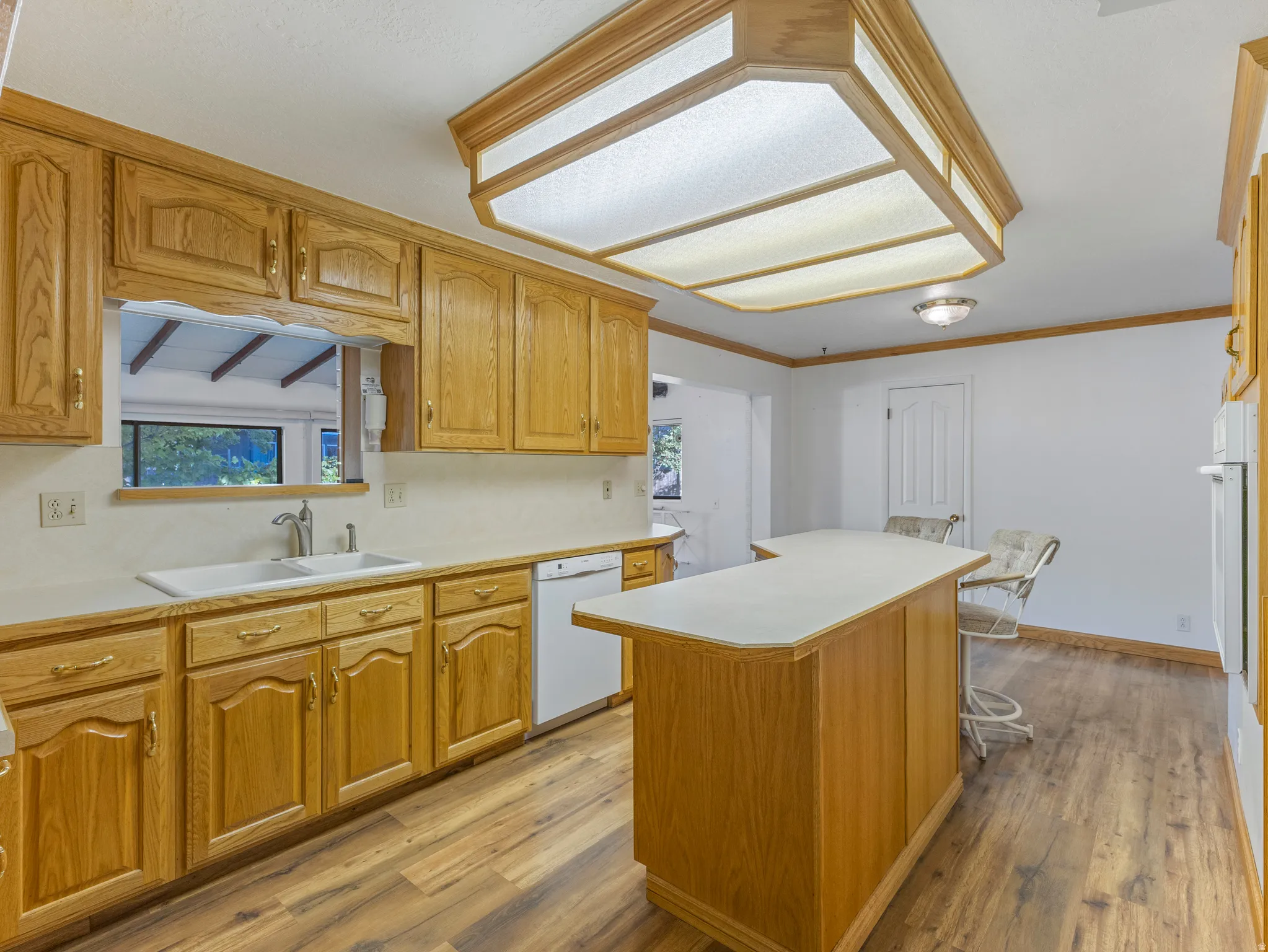 Kitchen featuring wood cabinetry, light countertops, wood-finish flooring, and a central island with seating