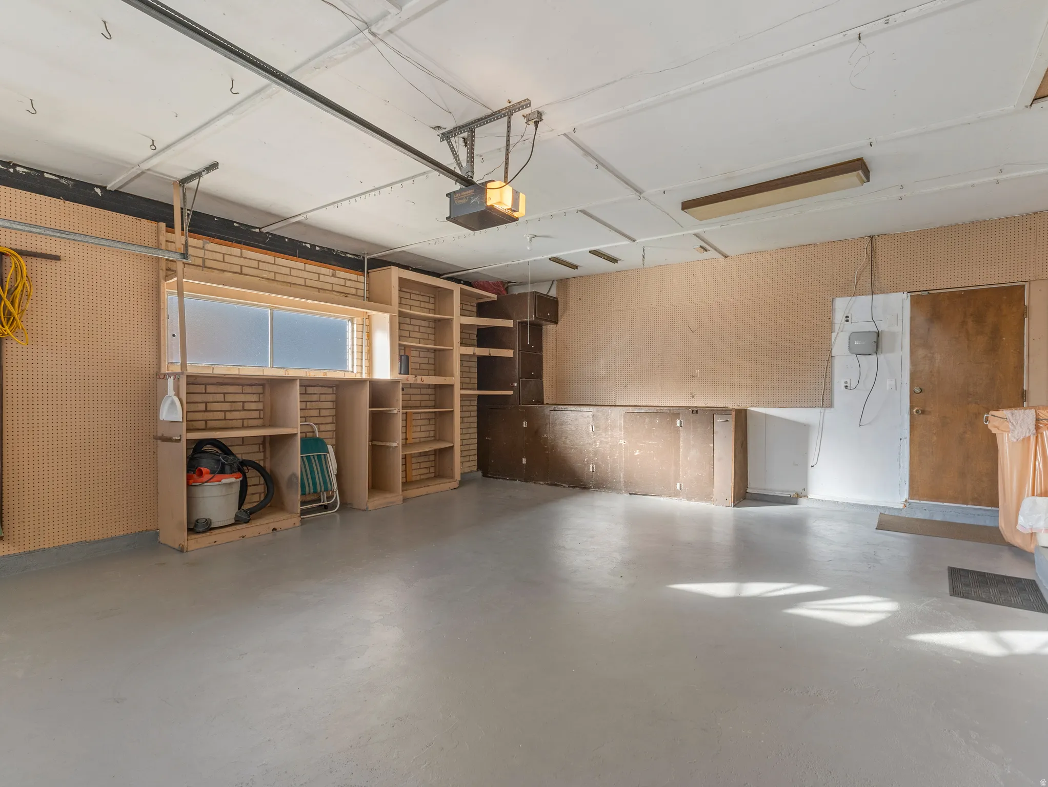 Spacious garage featuring a light gray epoxy floor, built-in shelving, brick accent wall, and a frosted glass window