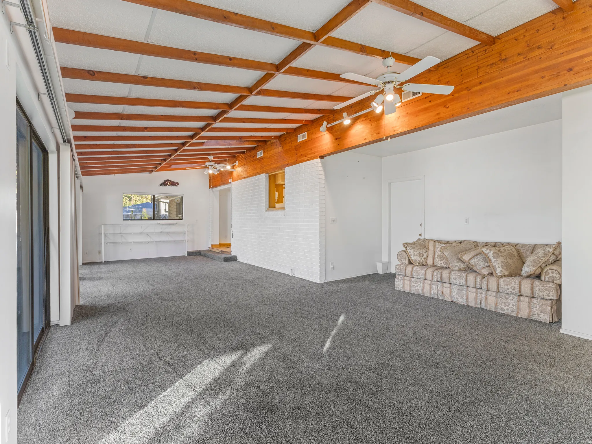 Spacious interior room featuring exposed wood ceiling beams, track lighting, and a white brick-finish wall