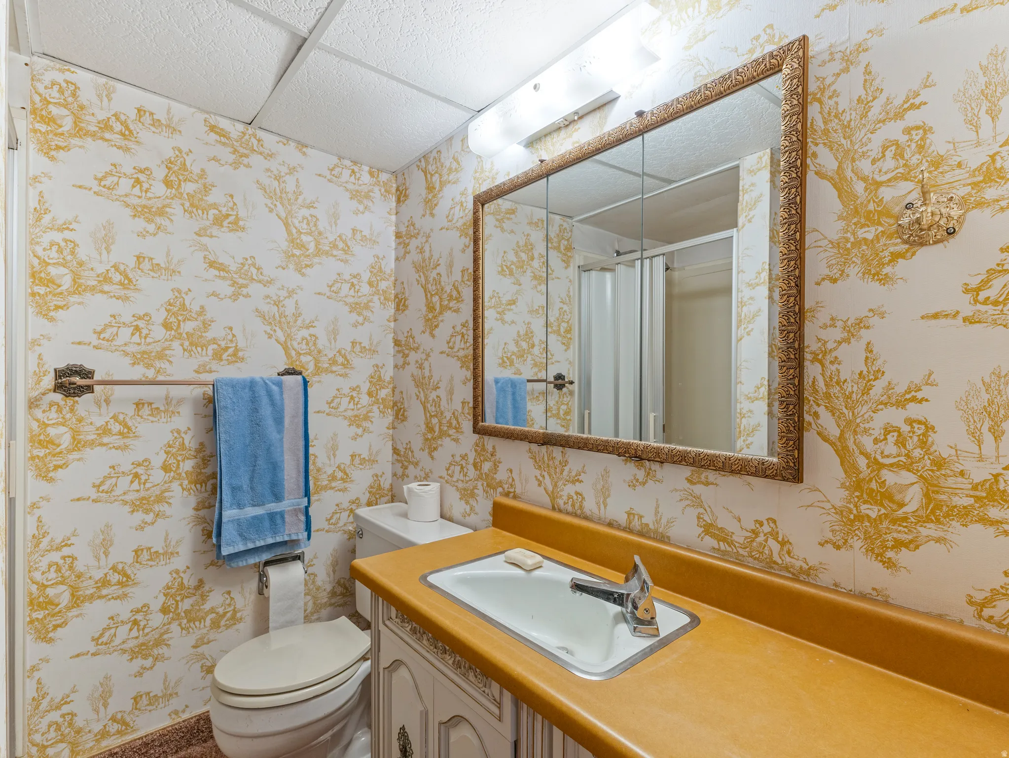 Bathroom featuring patterned wallpaper, a vanity with an integrated sink, a framed medicine cabinet, and a shower enclosure