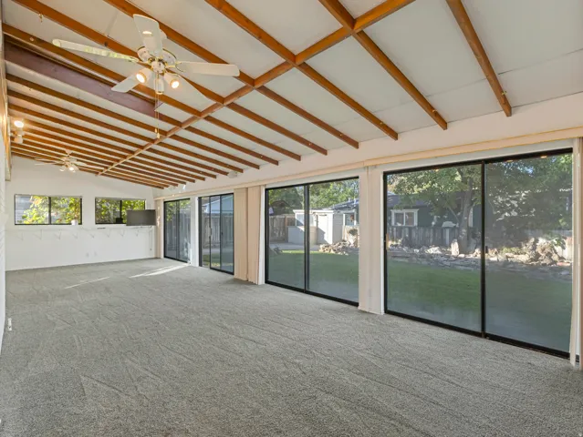 Spacious room with a vaulted ceiling featuring exposed wood beams and two ceiling fans