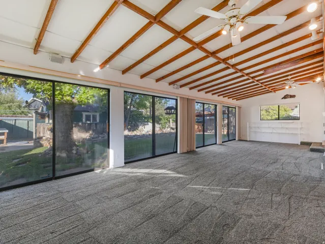 Expansive room featuring a vaulted ceiling with exposed wood beams, multiple ceiling fans, and track lighting