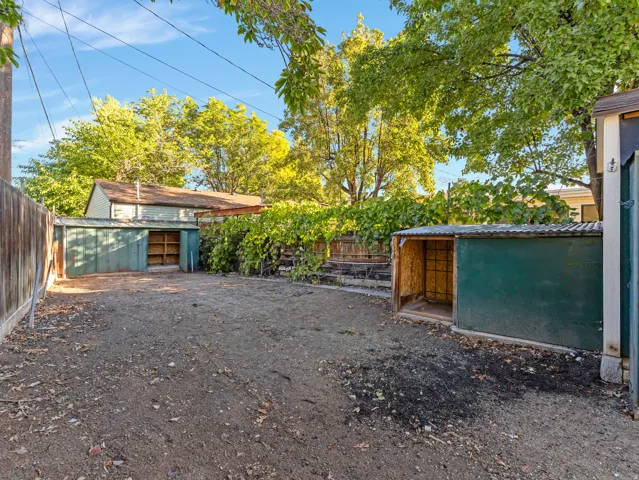 Expansive yard featuring two storage sheds with corrugated metal roofs, a wood fence, and mature trees providing natural screening
