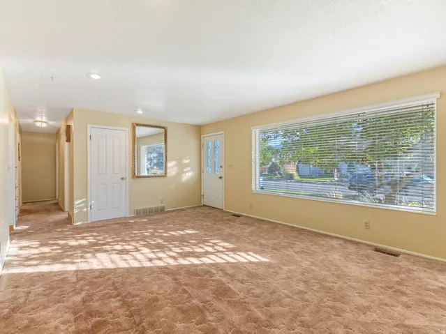 Expansive main living area featuring a large picture window with horizontal blinds, carpet flooring, recessed lighting, and a white paneled door