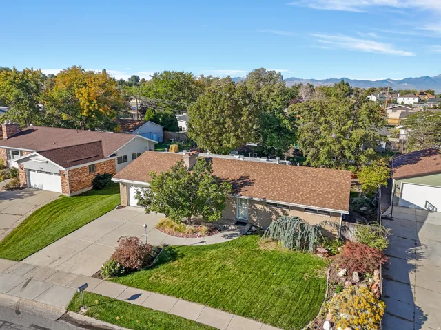 Brick exterior with a brown shingle roof, featuring an attached garage, paved driveway, and mature landscaping