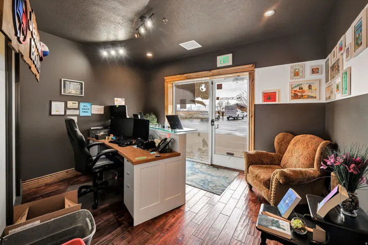 Wood-finish flooring throughout, featuring a reception desk with a light wood countertop, modern track lighting, and glass-paneled entry doors