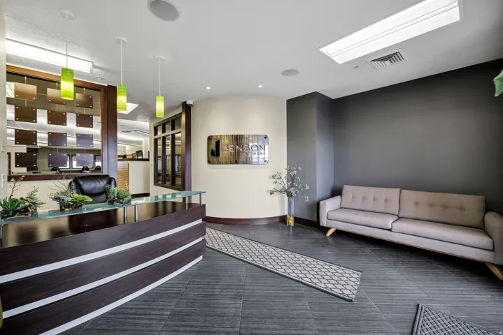 Contemporary reception area featuring dark wood-finish flooring, a curved reception desk with a glass top, and modern pendant lighting