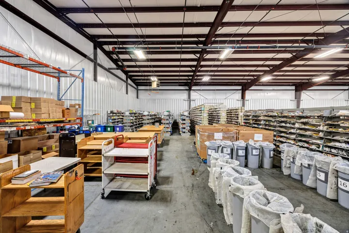 Expansive warehouse interior featuring high ceilings with exposed metal beams, fluorescent lighting, and durable concrete flooring