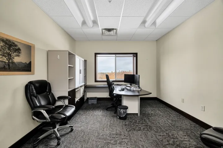Dedicated office space featuring a window, drop ceiling with fluorescent lighting, patterned carpet flooring, and dark baseboards