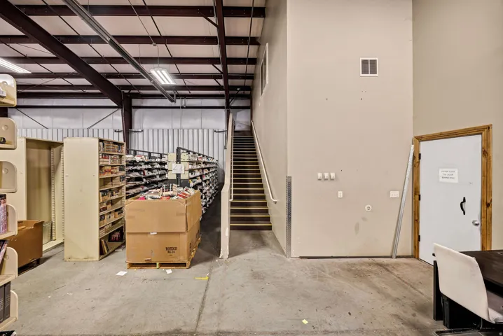 Spacious interior featuring a concrete floor, exposed metal beam ceiling, and a prominent staircase with metal railing