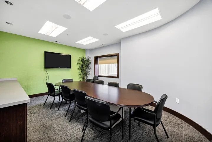 Conference room featuring an oval wood-finish table, wall-mounted television, textured accent wall, and recessed lighting