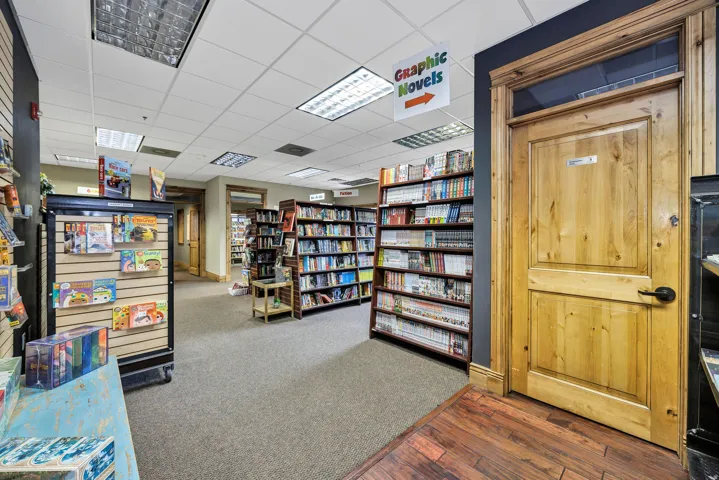 Commercial interior featuring wood-finish flooring, drop ceiling with recessed lighting, and a solid wood door with dark hardware