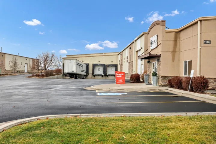 Commercial property featuring a stucco and stone facade, multiple loading docks, an expansive asphalt parking lot, and manicured landscaping
