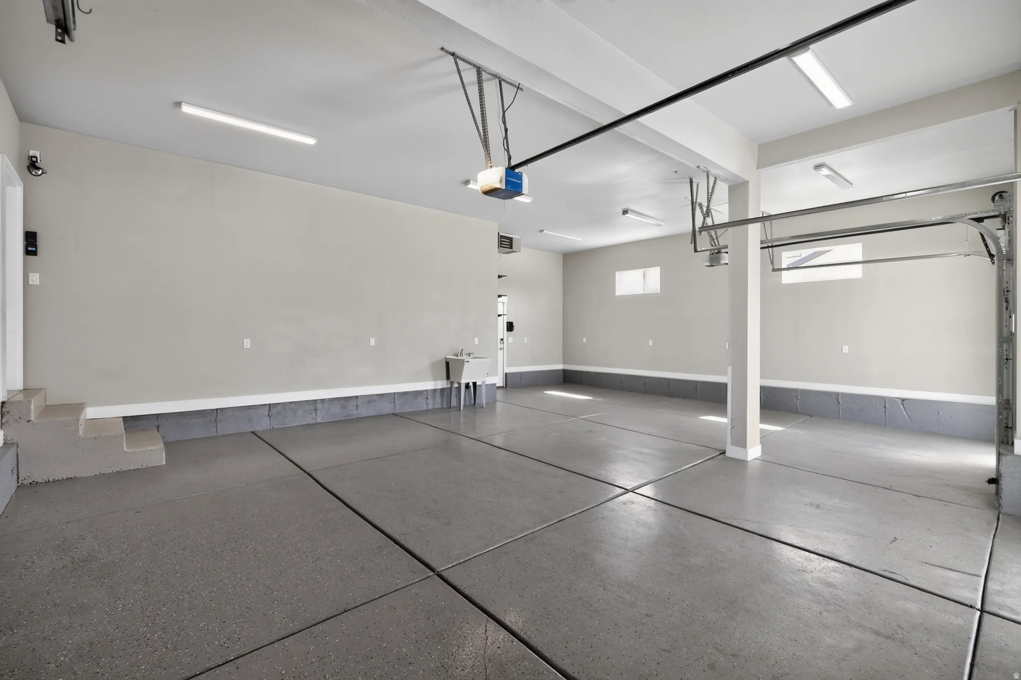 Spacious garage featuring a finished concrete floor, utility sink, interior access door, recessed windows, and overhead lighting