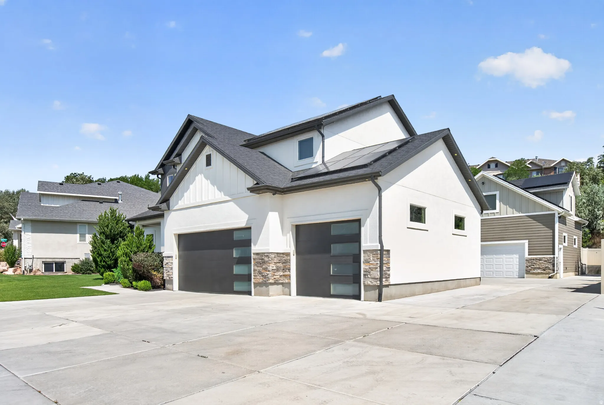 Contemporary residence featuring a white stucco exterior, dark shingle roof, and stone accents