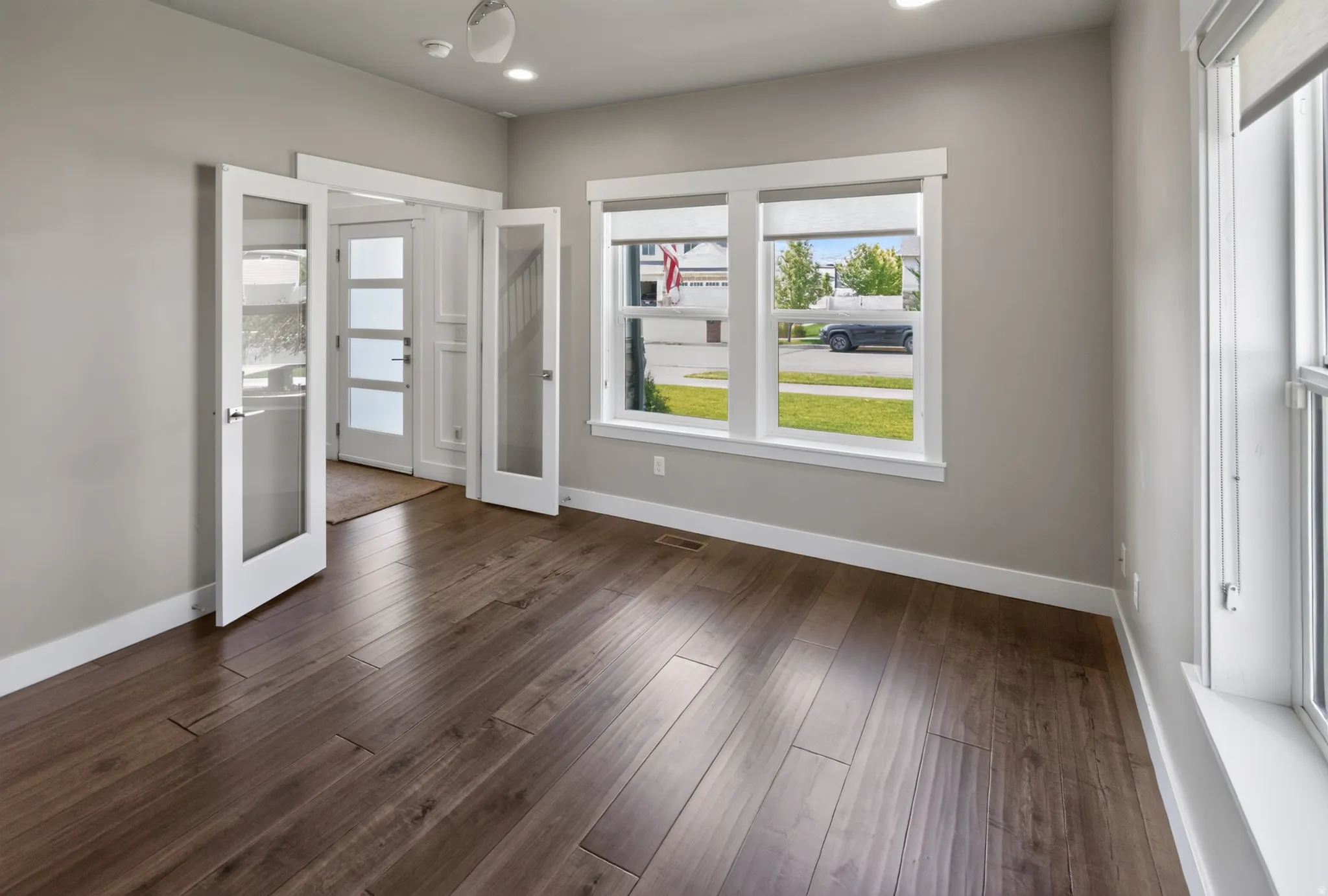Open room featuring wood-finish flooring, two sets of glass-paneled double doors, and multiple windows