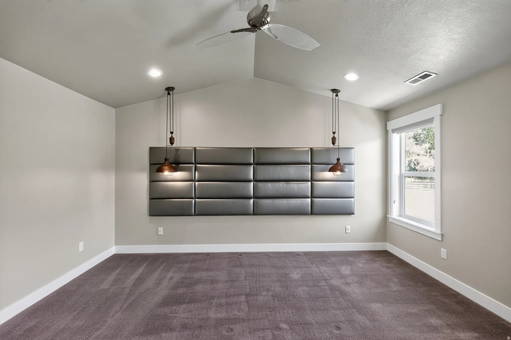 Spacious room featuring a vaulted ceiling with a ceiling fan, plush carpet flooring, and a window with white trim