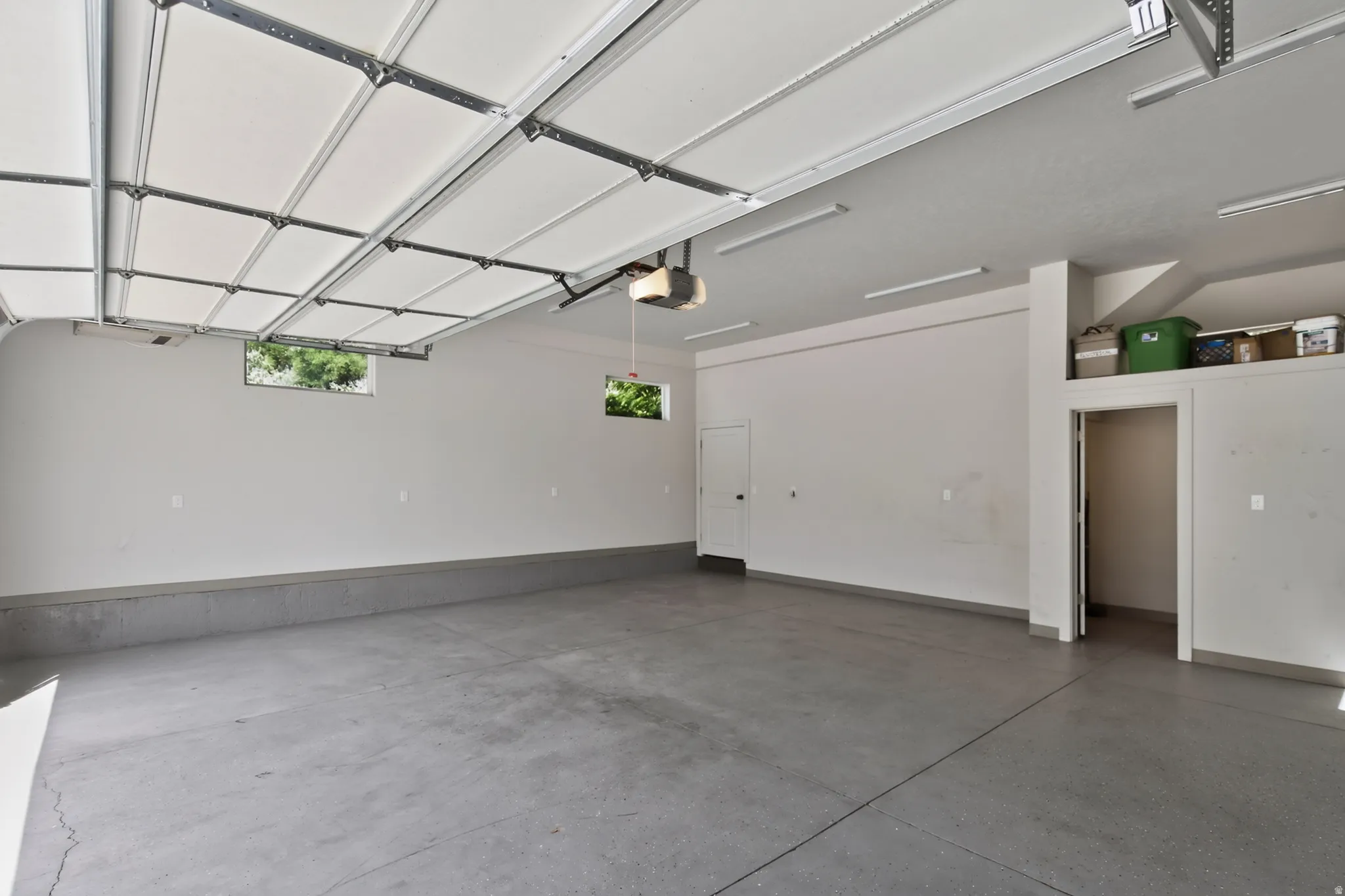 Spacious garage featuring a durable concrete floor, two windows providing natural illumination, overhead fluorescent lighting, and a built-in storage alcove