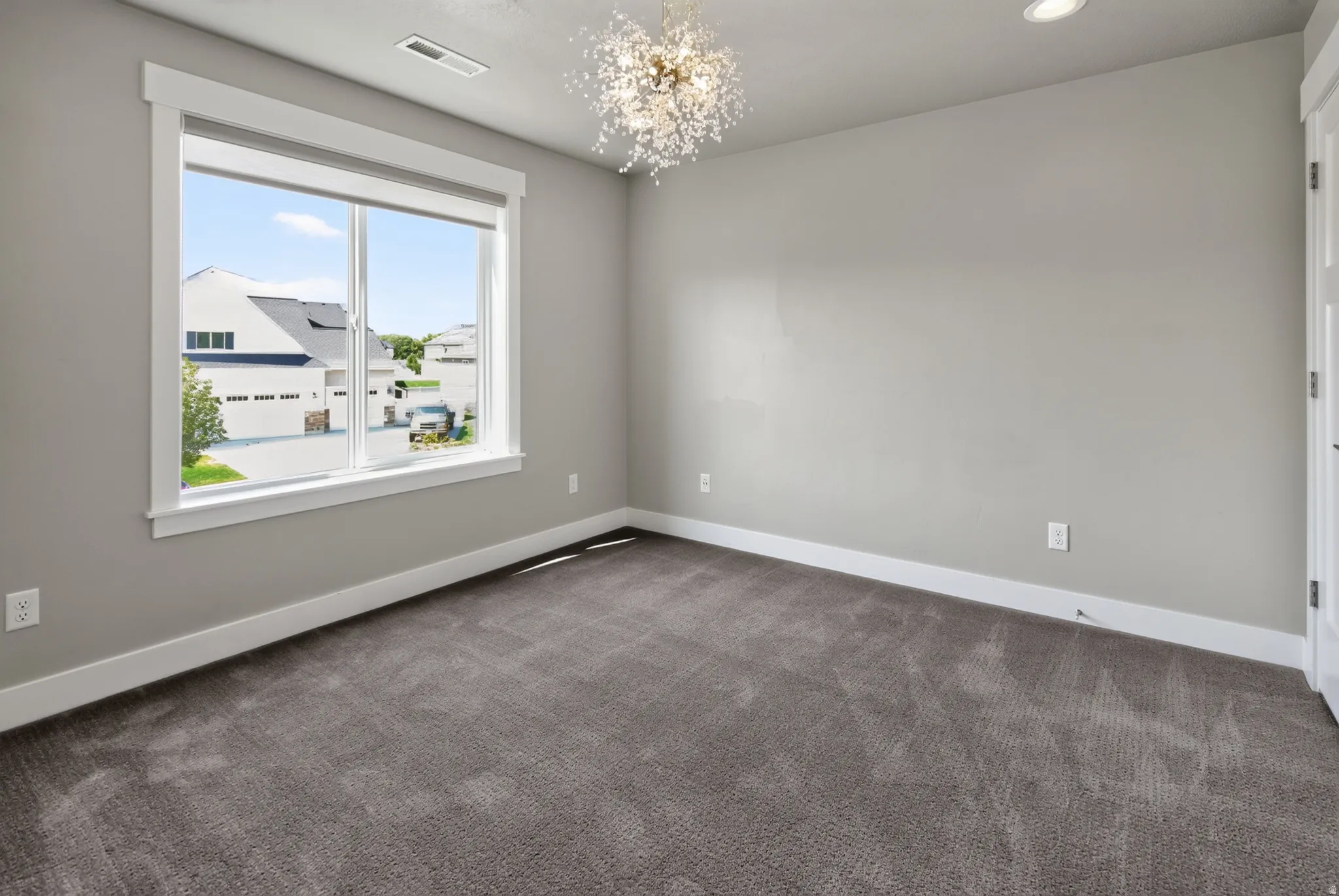 Light gray wall paint with white trim, gray carpet, and a modern chandelier