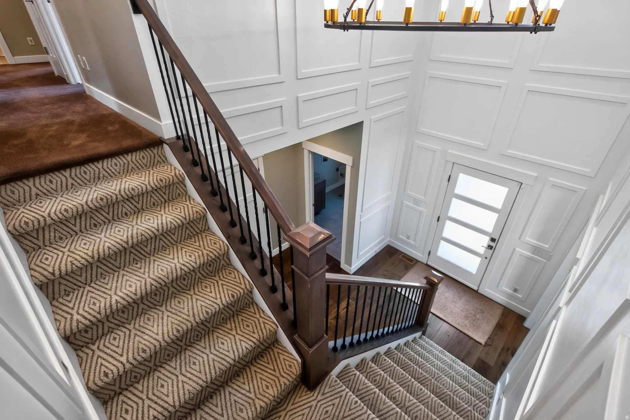 Foyer featuring a two-story ceiling, decorative wall paneling, a modern chandelier with brass accents, a front door with multiple frosted glass panels, and dark wood-finish flooring