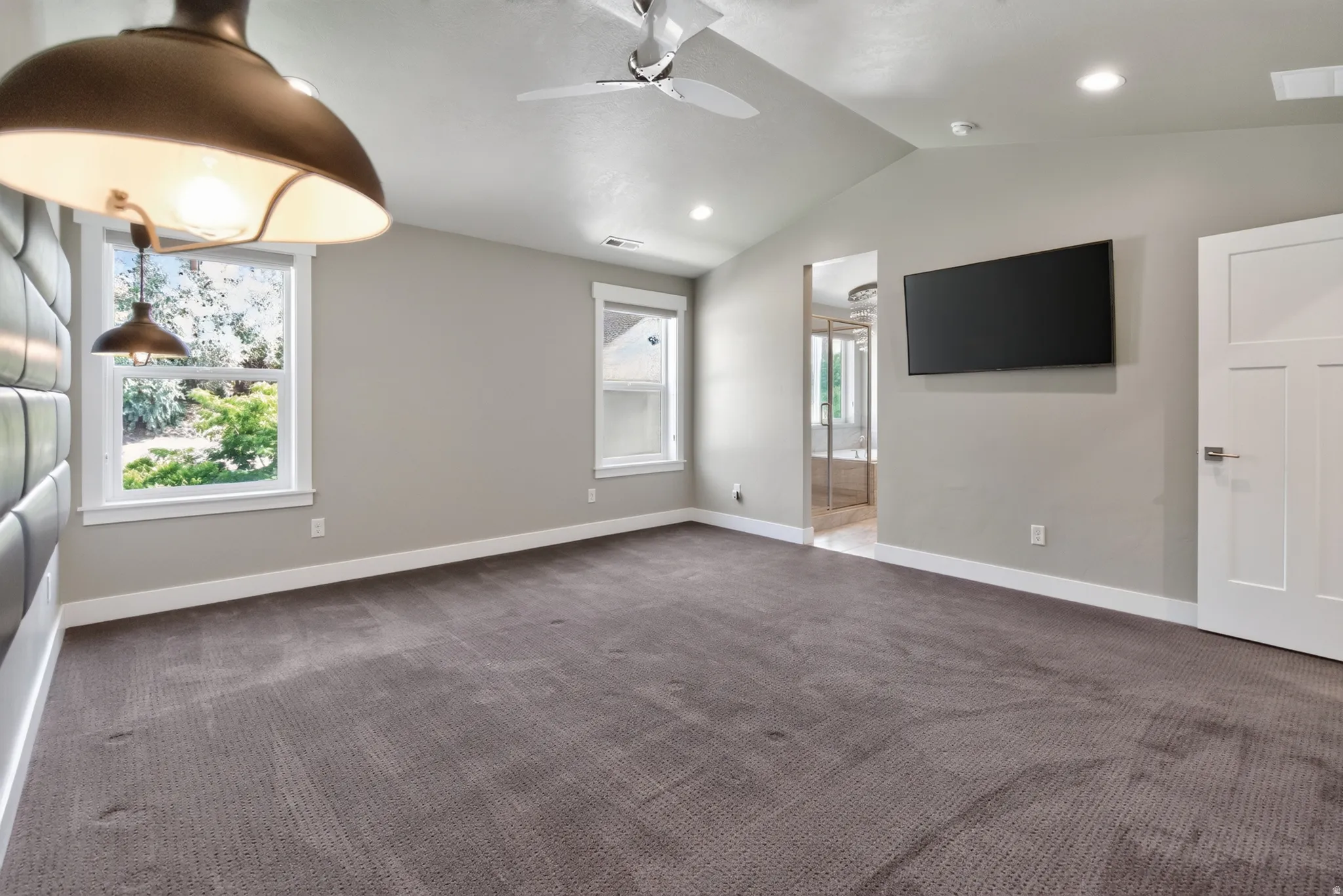 Spacious room featuring vaulted ceilings, recessed lighting, soft gray walls, and plush carpet flooring