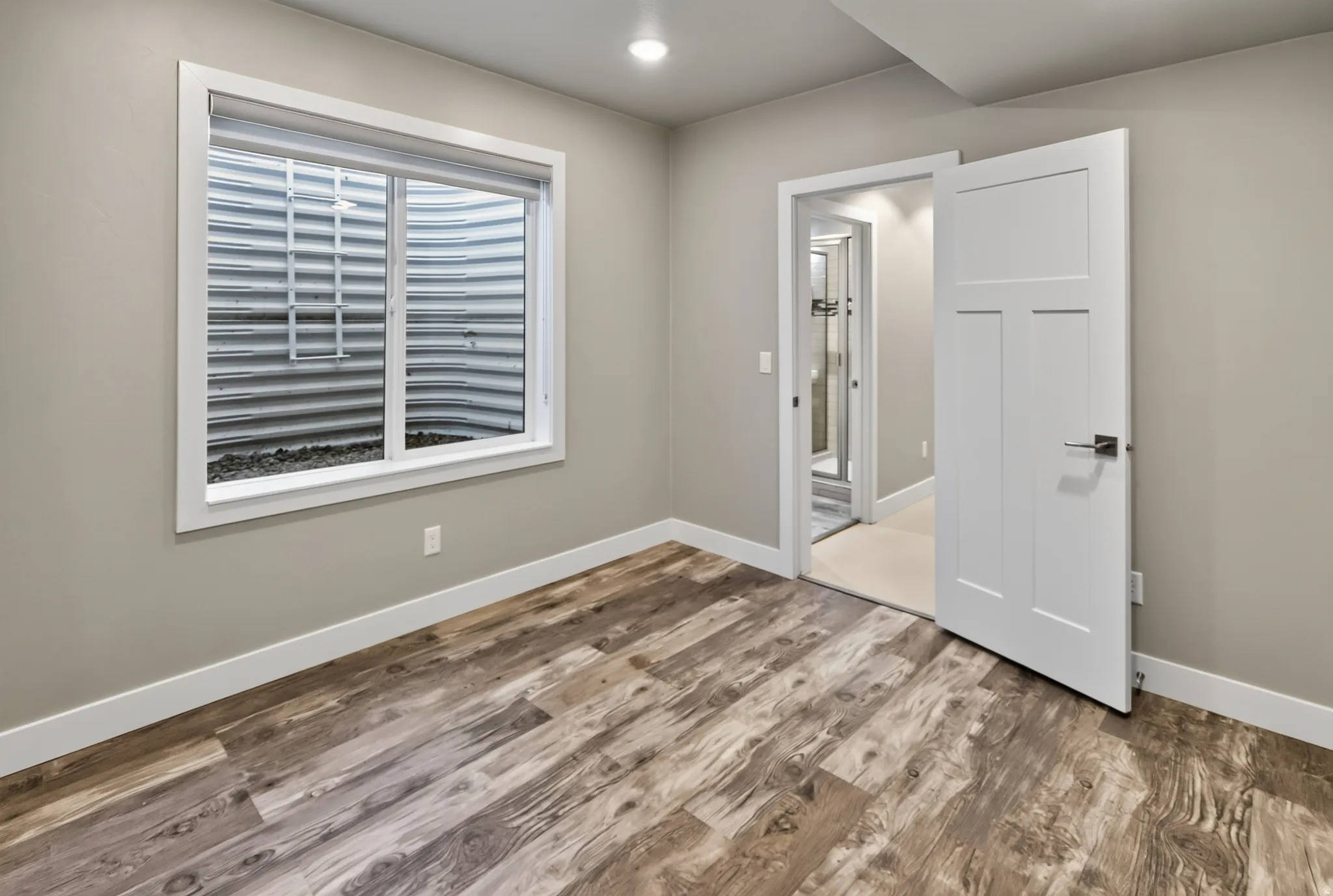 Room featuring wood-finish flooring, a white trim window, recessed lighting, and a contemporary panel door with a lever handle