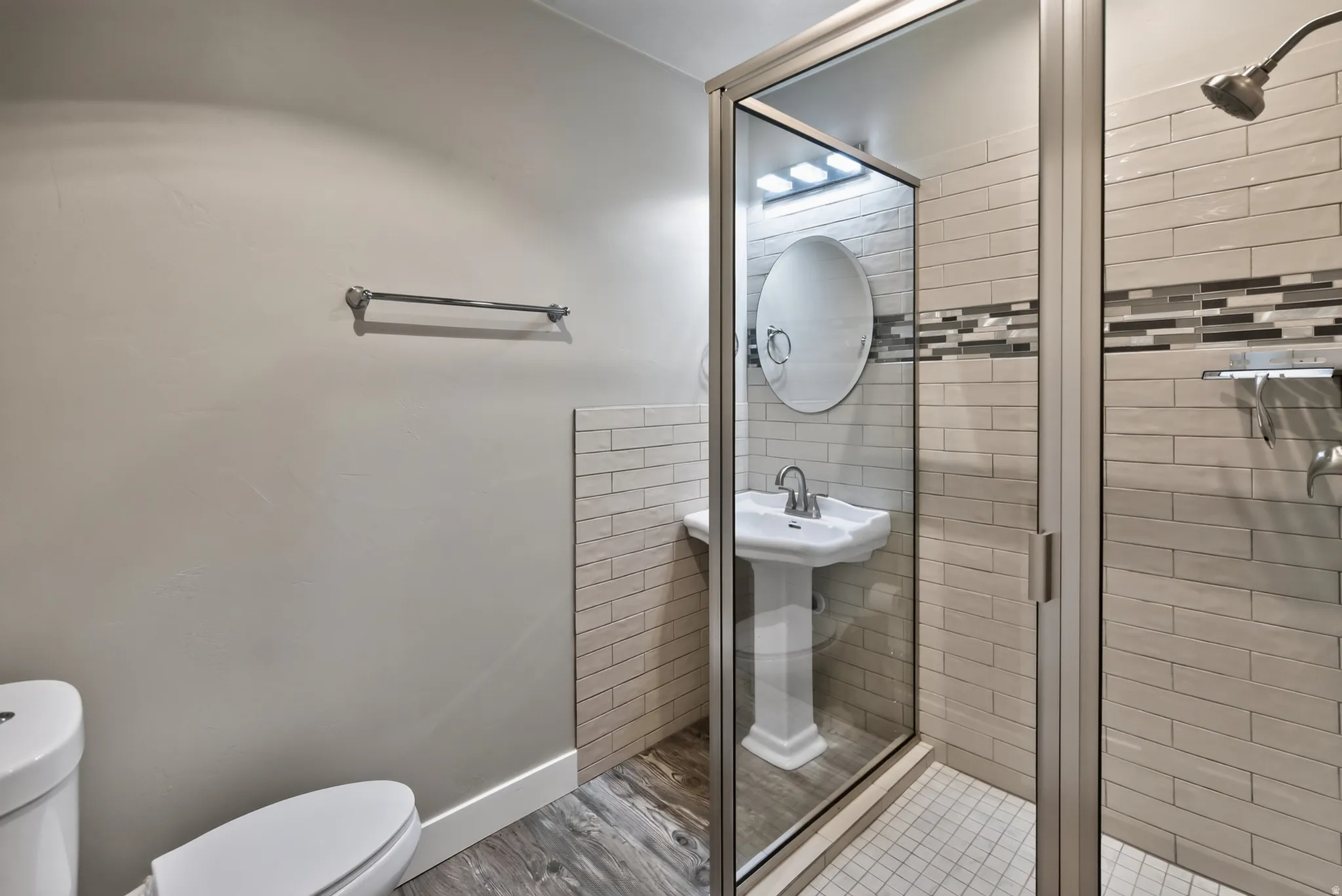 Bathroom featuring a glass-enclosed shower, pedestal sink with oval mirror, and horizontal tilework with a decorative accent band