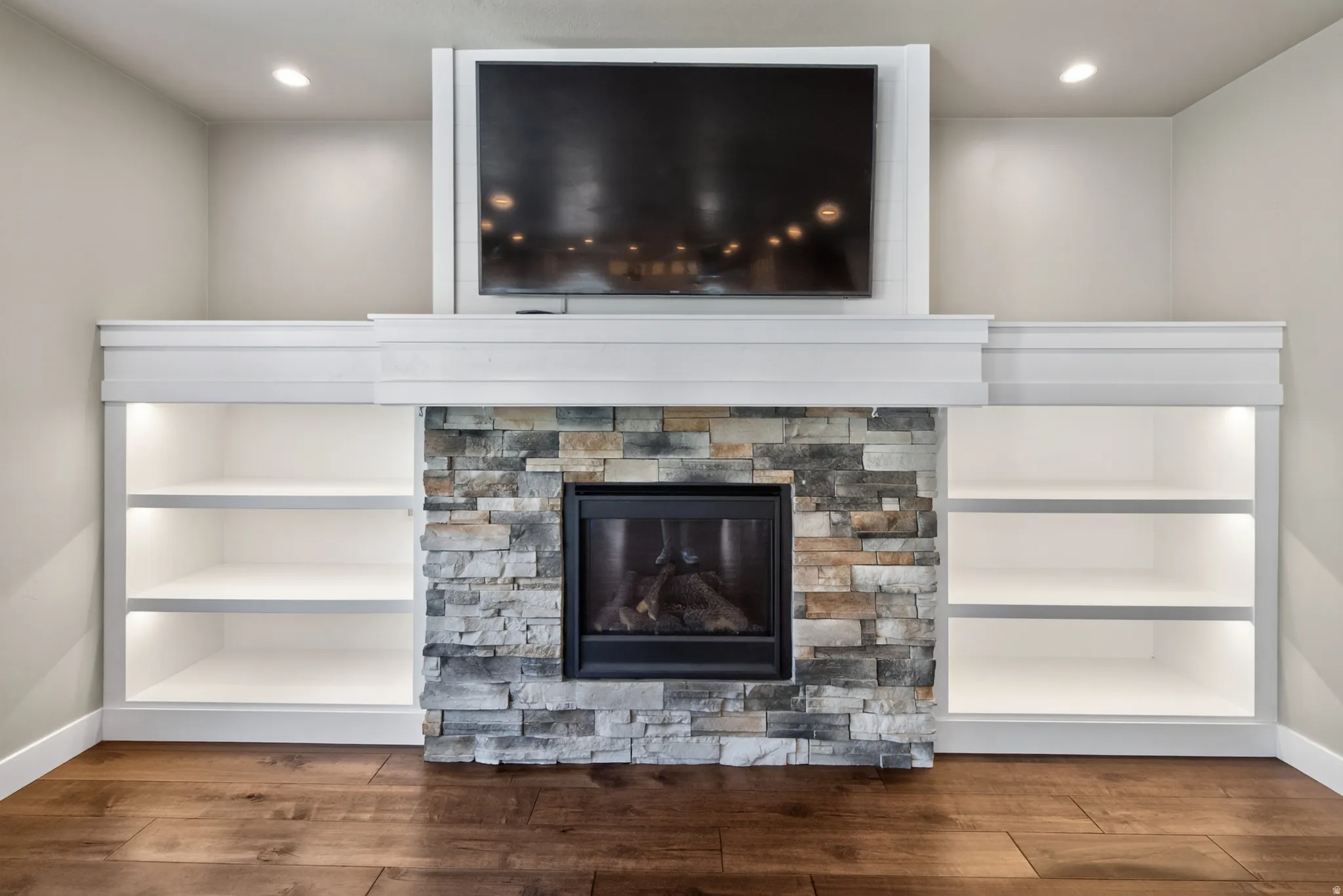 Stone-faced fireplace with a black firebox, flanked by custom built-in shelving with integrated lighting, and topped by a white mantelpiece and trim