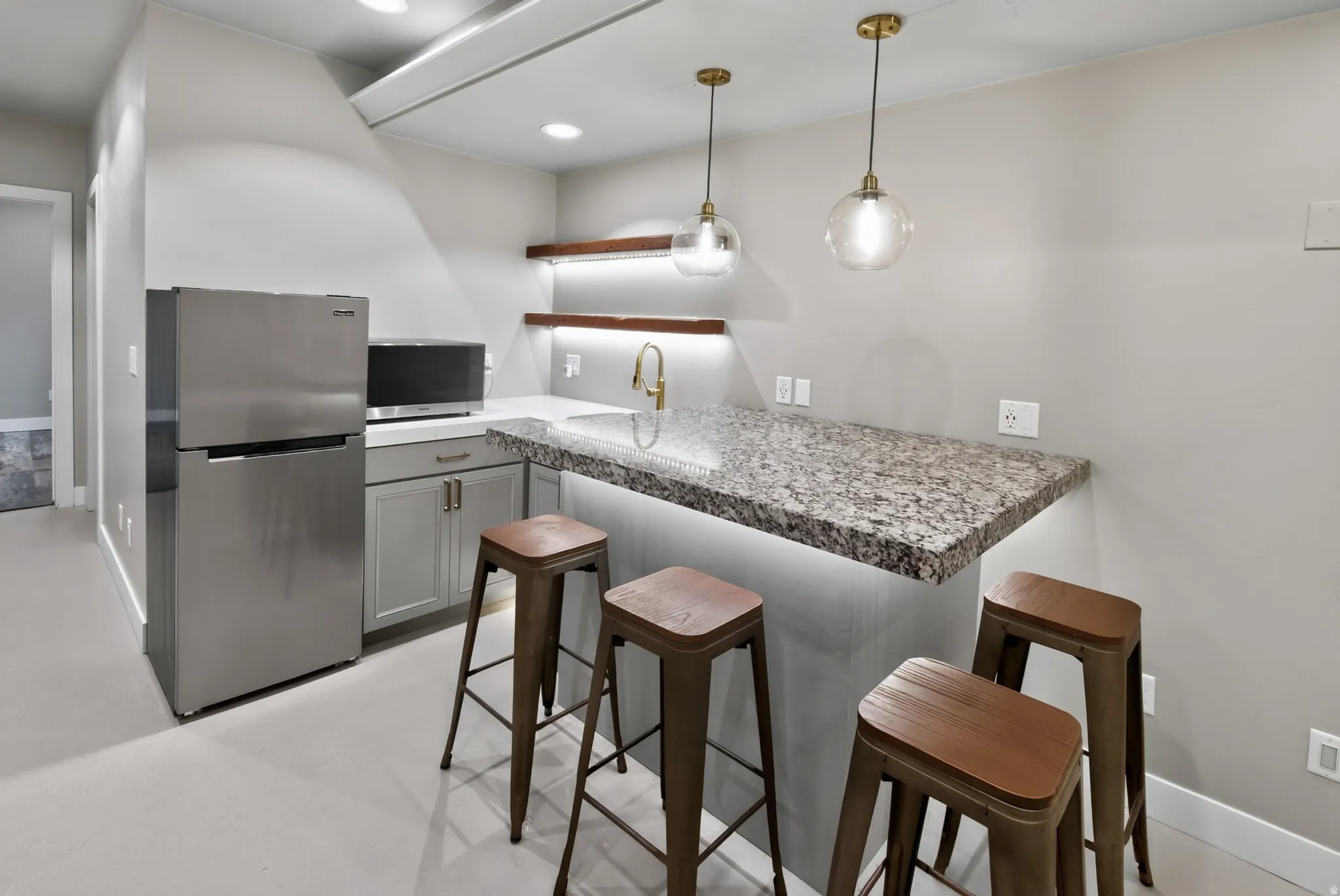 Contemporary kitchenette featuring a granite countertop, undermount sink with brass-finish faucet, under-cabinet lighting, and stainless steel appliances