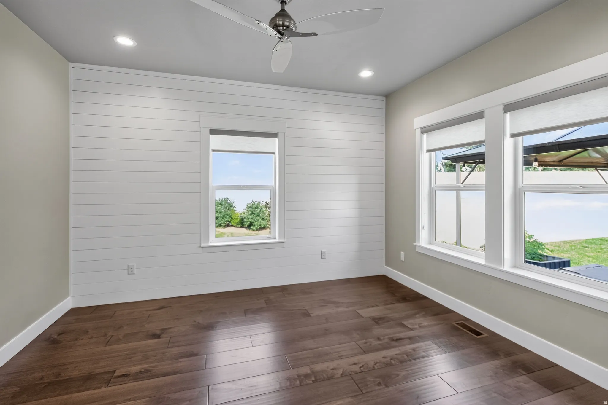 Spacious interior featuring wood-finish flooring, a contemporary ceiling fan, recessed lighting, and multiple windows with roller shades