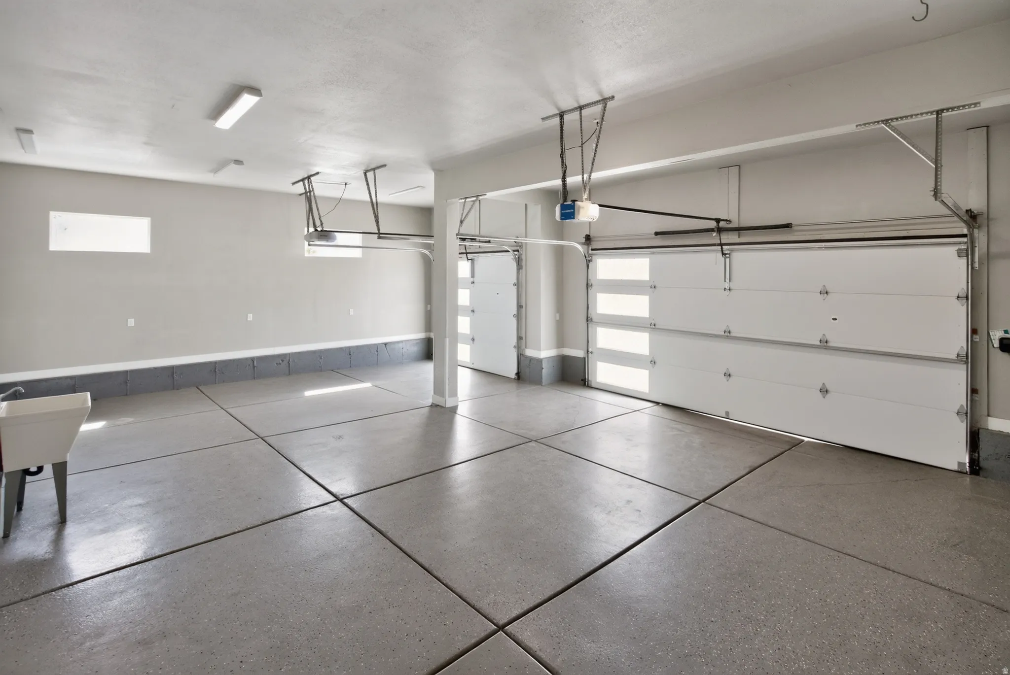 Spacious three-car garage featuring segmented garage doors with integrated window panels, an epoxy-coated concrete floor, and multiple overhead fluorescent light fixtures