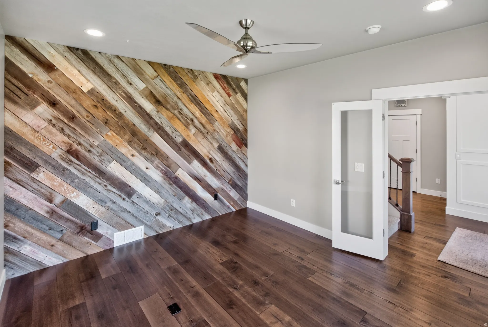 Reclaimed wood accent wall with diagonal planking, rich wood-finish flooring, recessed lighting, and a ceiling fan