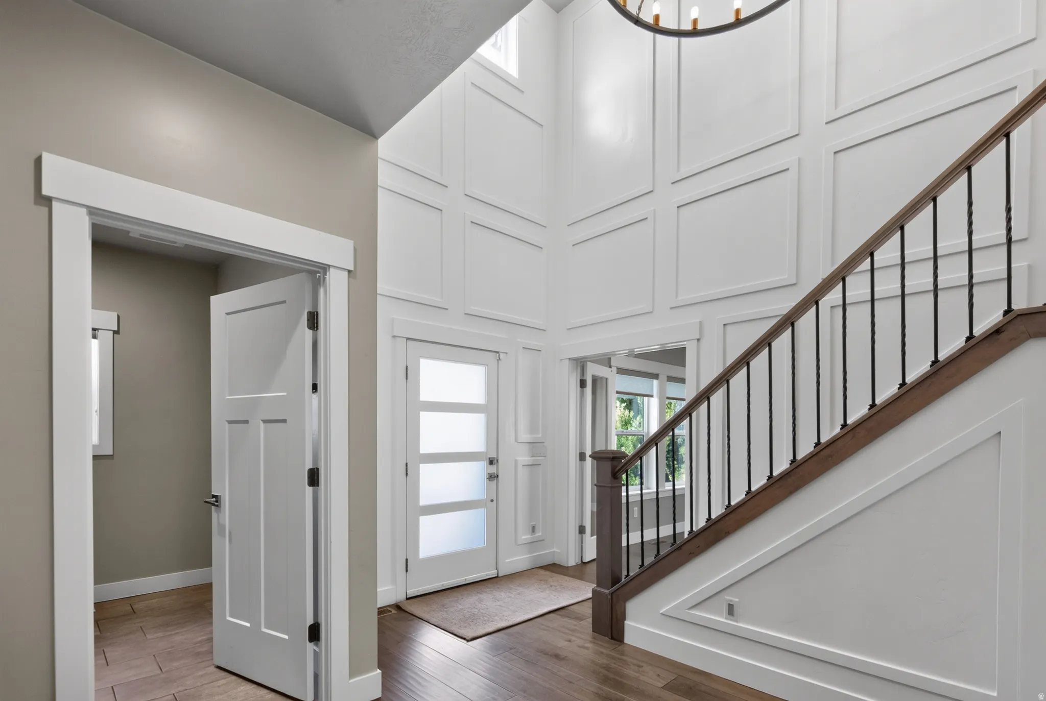 Two-story foyer featuring wainscoting, a hardwood staircase with wrought iron balusters, and a contemporary chandelier