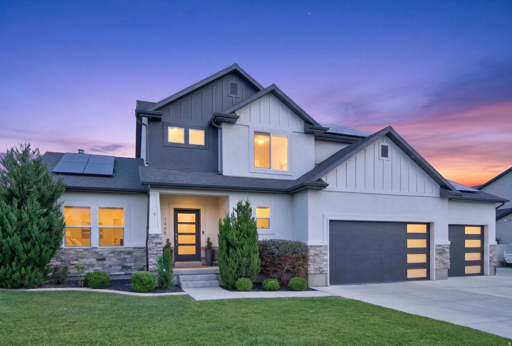 Modern architectural style featuring a multi-story design with a combination of light and dark siding, stone veneer accents, and a dark shingle roof