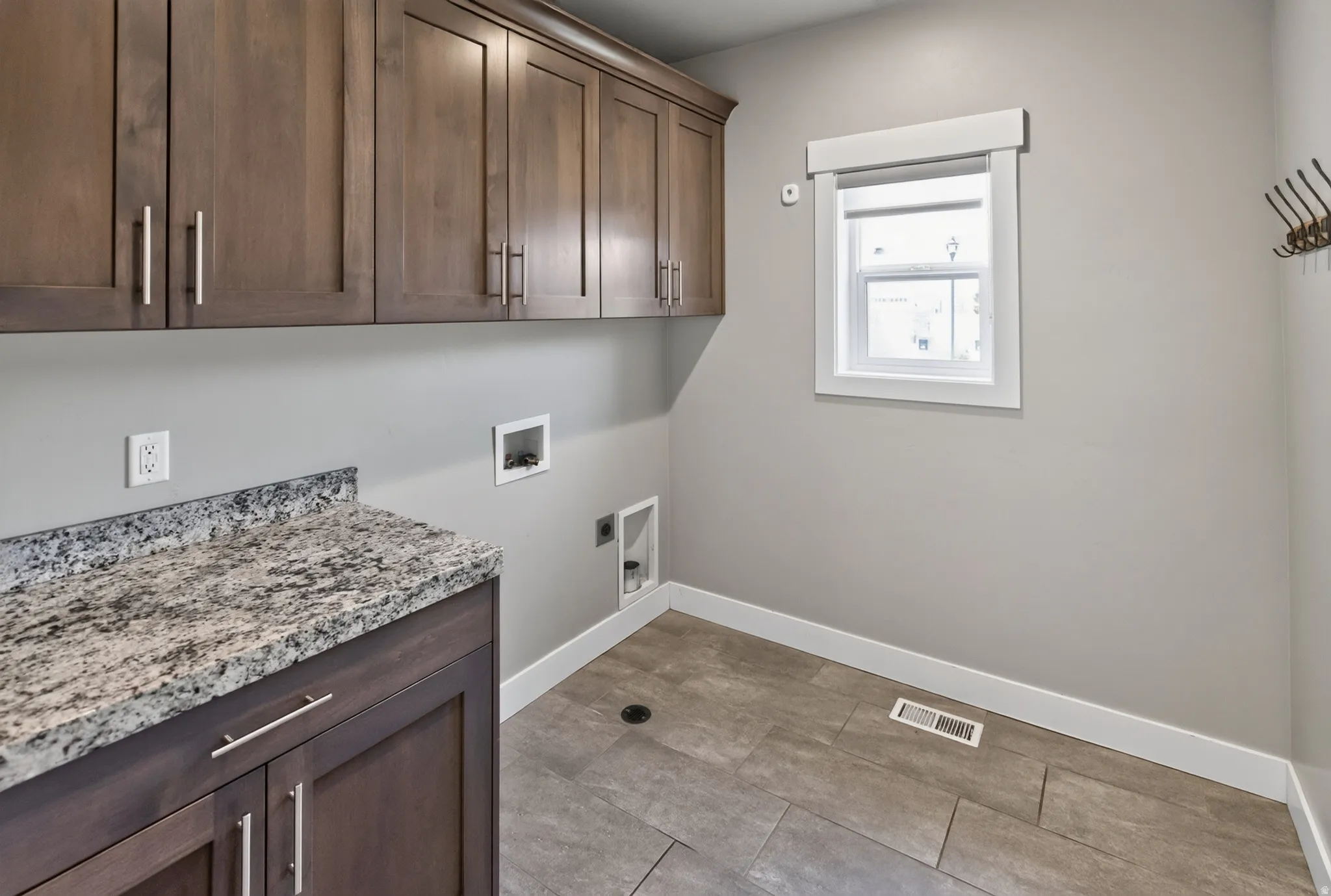 Functional utility space featuring wood-finish cabinetry, a speckled countertop, and tiled flooring