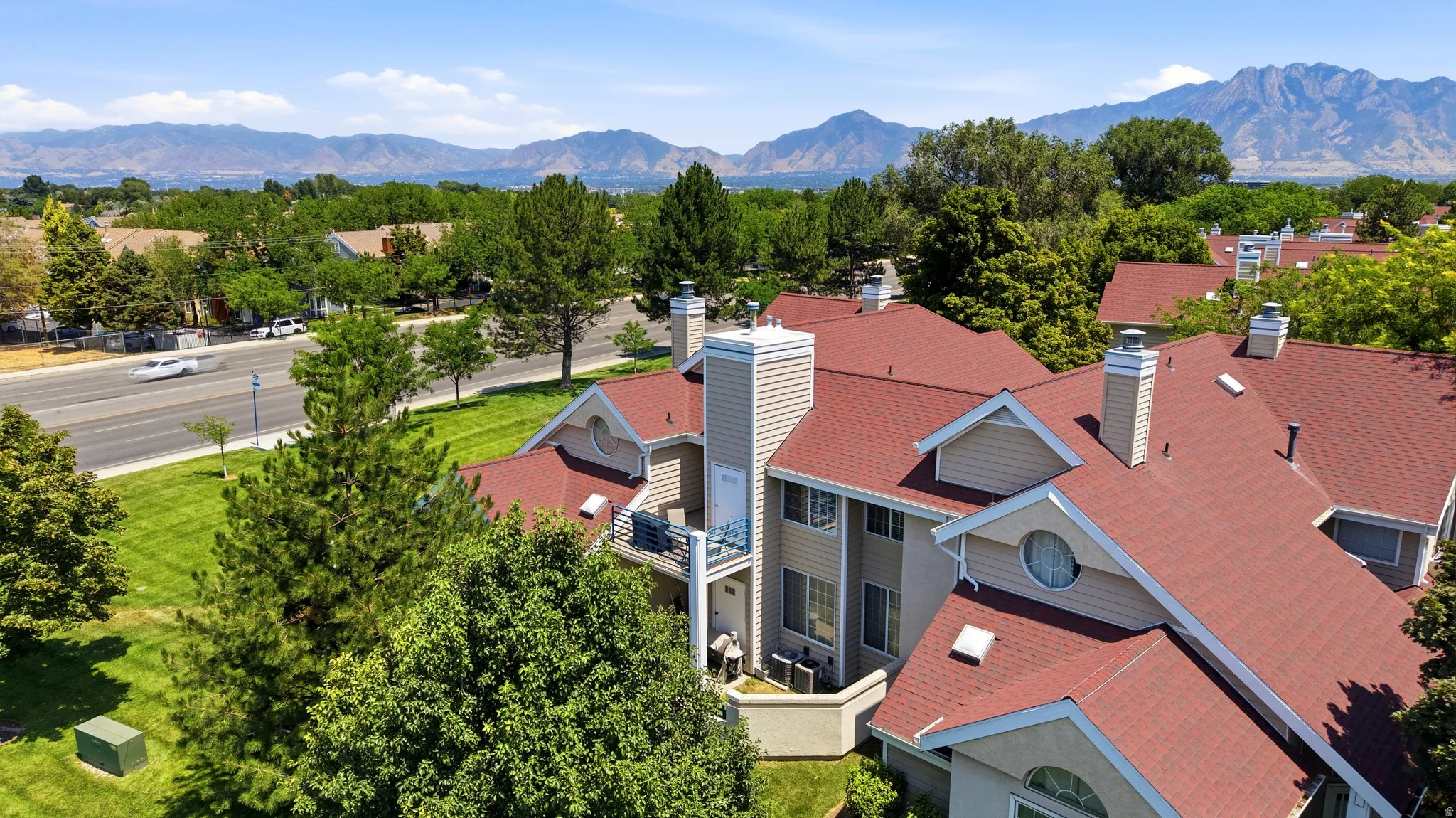Multi-story residential building featuring red shingle roofing, light-colored siding, multiple balconies, and prominent chimney structures