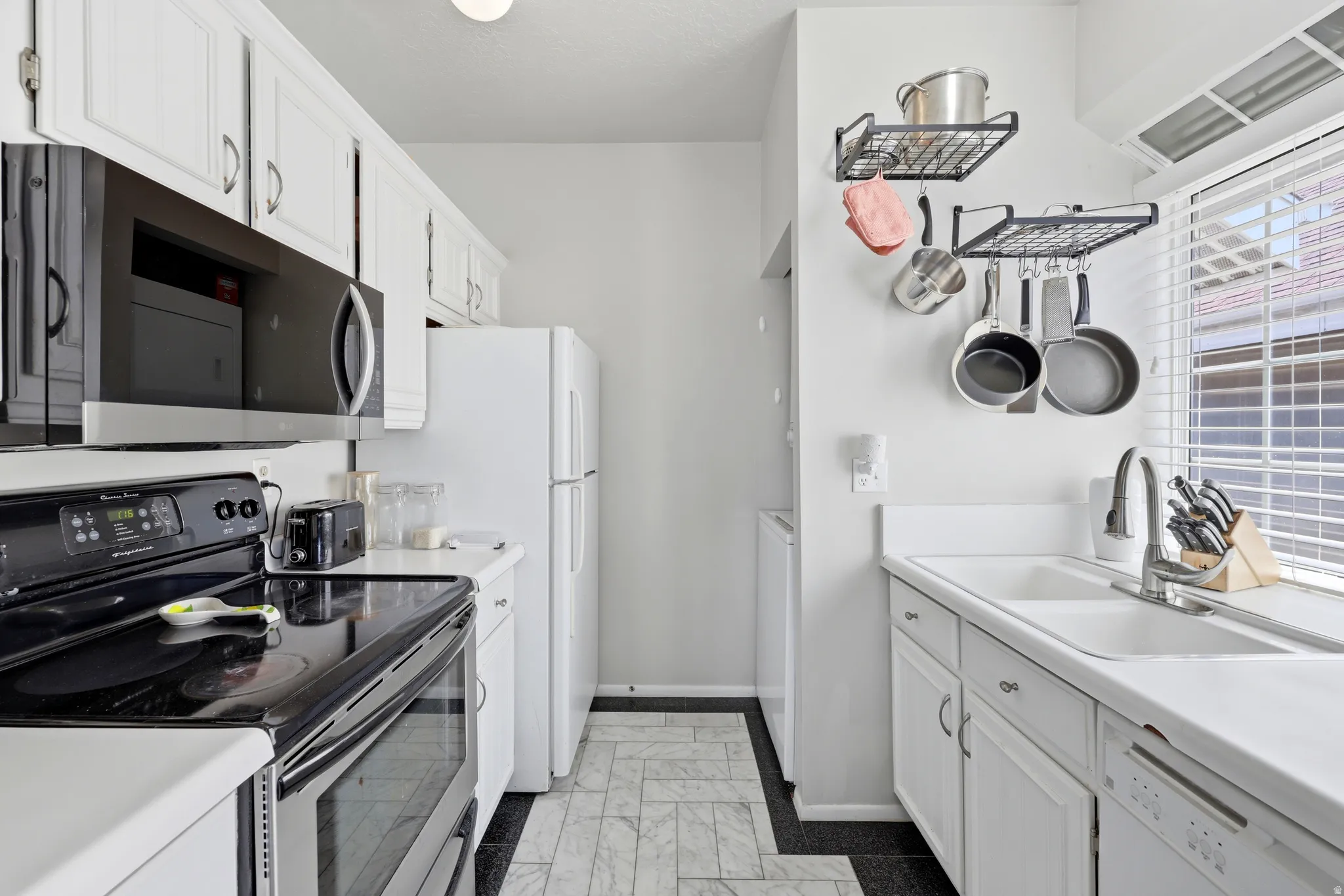 Galley-style kitchen featuring white cabinetry, an electric range, built-in microwave, and a double-basin sink