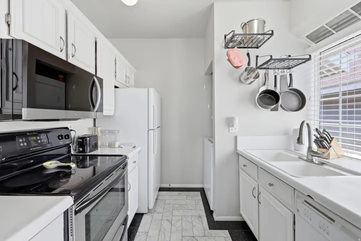 Galley-style kitchen featuring white cabinetry, an electric range, built-in microwave, and a double-basin sink