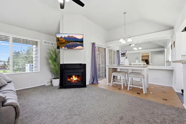 Living area featuring a corner fireplace with a black surround, vaulted ceilings, and large windows with horizontal blinds