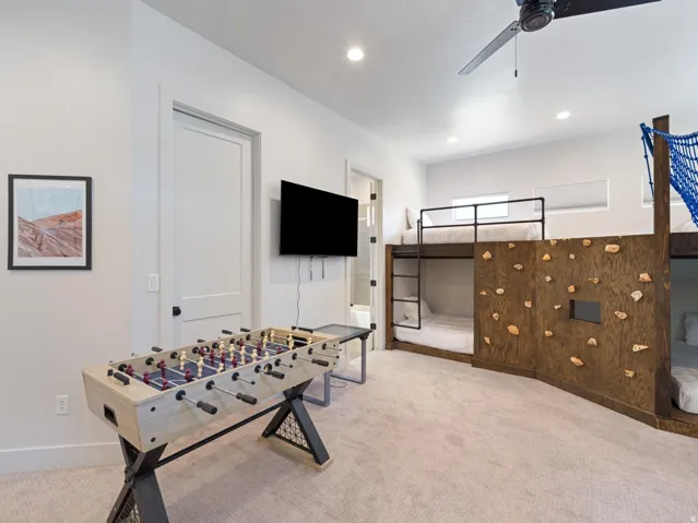 Built-in bunk beds with integrated ladder and climbing wall, mounted television, recessed lighting, and a ceiling fan