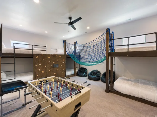Spacious room featuring multiple built-in bunk beds with dark wood frames and metal railings, a climbing wall with handholds, and a ceiling fan