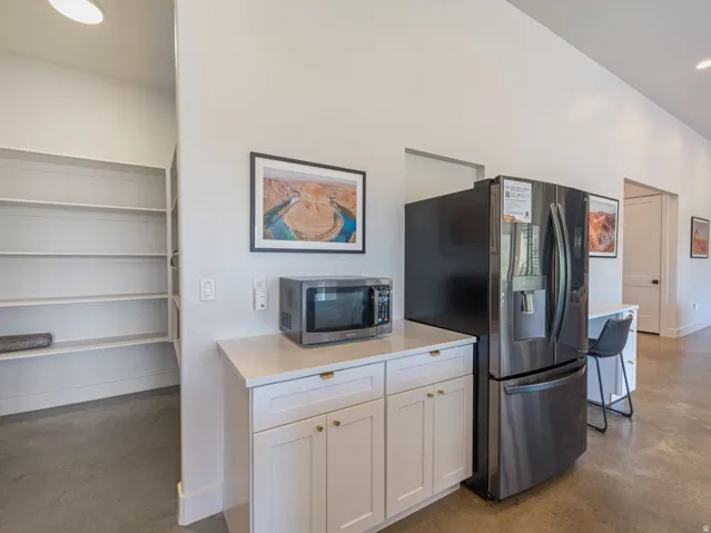 Kitchenette featuring white cabinetry with gold-tone hardware, a light-toned countertop, and concrete flooring