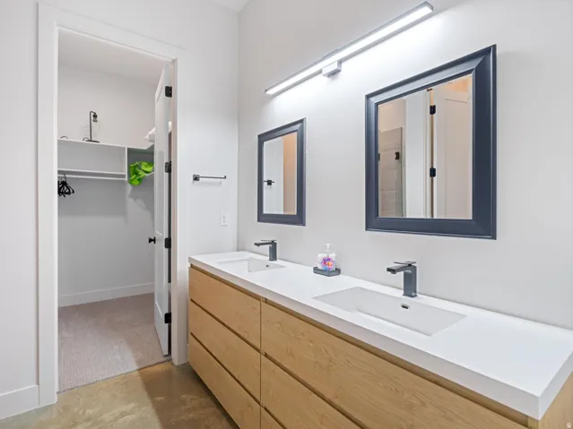 Double vanity featuring light wood-finish cabinetry, integrated rectangular sinks, and matte black fixtures