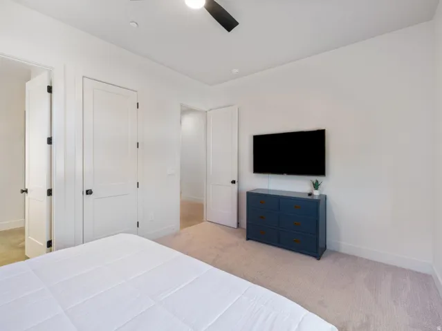 Carpeted room featuring white walls, a ceiling fan, and white doors with matte black hardware
