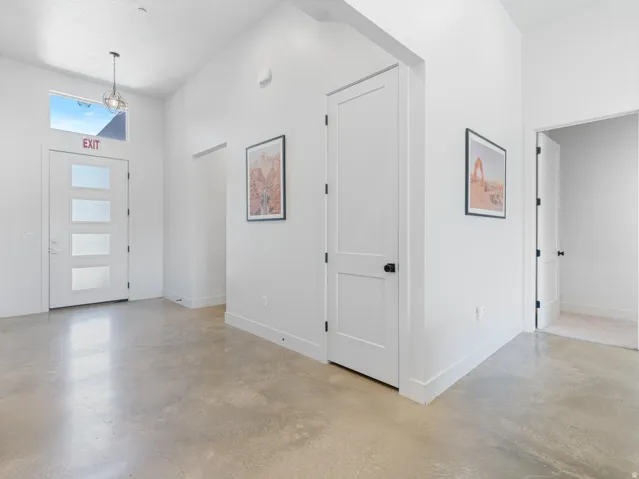 Entryway featuring vaulted ceilings, polished concrete flooring, contemporary pendant lighting, and a modern white door with frosted glass panels