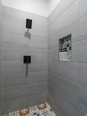 Shower with grey rectangular wall tiling, a built-in niche with decorative tiling, and a patterned floor with geometric and floral motifs