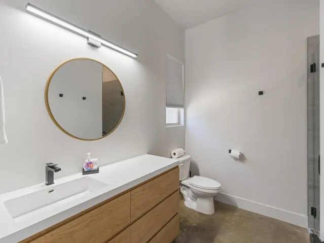 Modern bathroom featuring a wood-finish vanity with an integrated rectangular sink, matte black faucet, and a round wall-mounted mirror